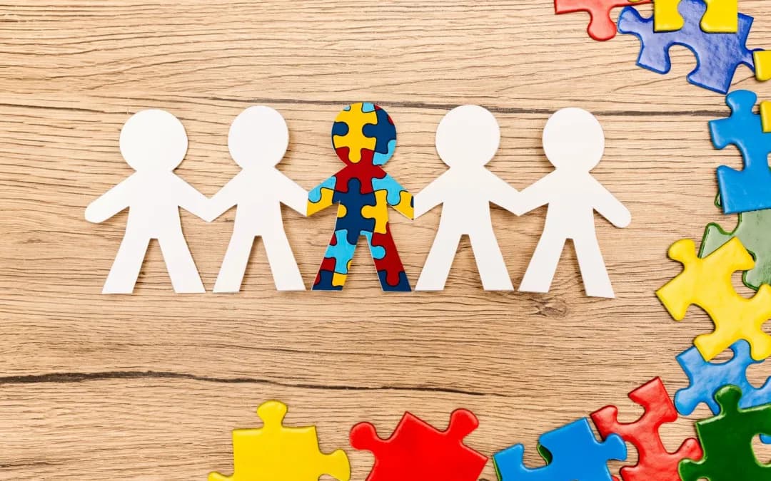 Paper people holding hands, with a central figure patterned in colorful puzzle pieces.